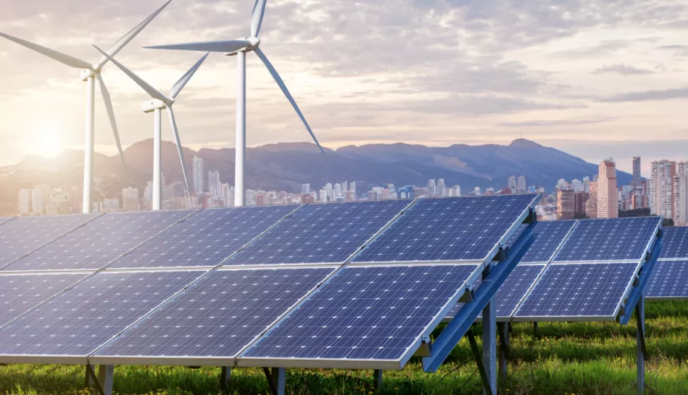 Solar panels and wind turbines against the backdrop of a city and mountains at sunset